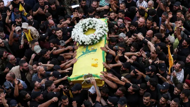 A crowd of people holding a coffin draped in yellow