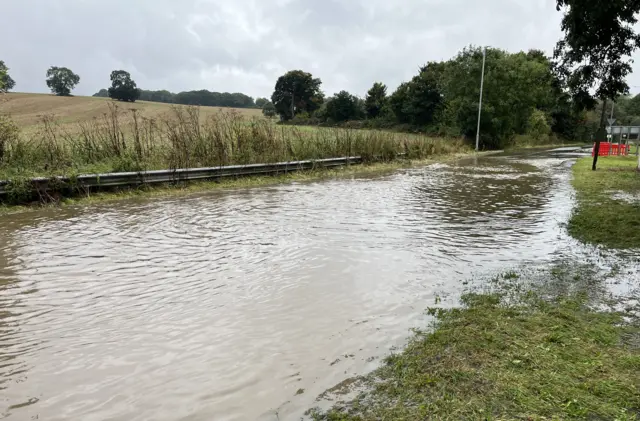 A photo shows flood water that has submerged a road in Dunstable. The road's verges have also been submerged. The water stretches about hundred metres.