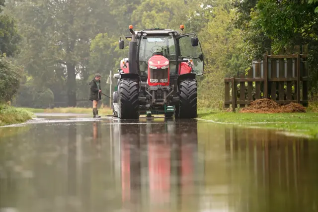 A man in Wellington boots, standing next to a red and black tractor.