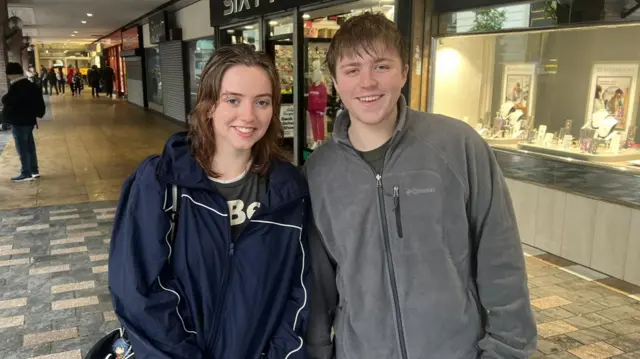 Sophie and Martin shopping in Liverpool city centre. Sophie has shoulder-length brown hair and wears a blue sports jacket. Martin has short brown hair and wears a grey fleece.