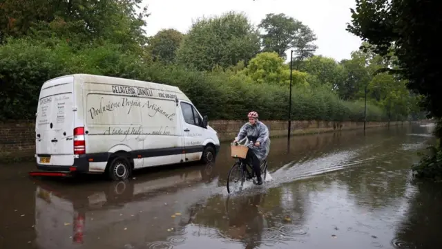 A person cycles through floodwater as heavy rain combines with the overtopping of the river bank of the tidal River Thames on a road in west London, Britain, September 23, 2024.