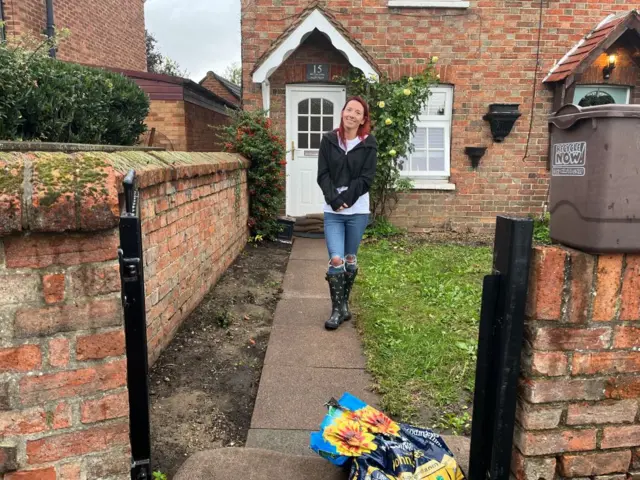 Emma Pearce in front of her terraced home. She is wearing wellington boots and there are sandbags in front of her garden gate.