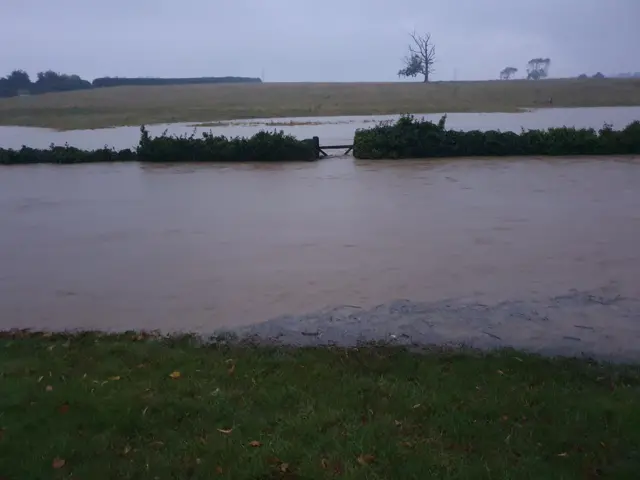 A flooded field in Easton Maudit, with a hedgerow and the top of a barred gate visible above the water