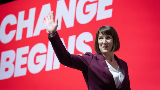 Rachel Reeves, wearing a burgundy suit, waves at the crowd inside the main hall at Labour conference before giving her speech