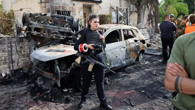 A member of the Israeli security forces stands next to a charred car