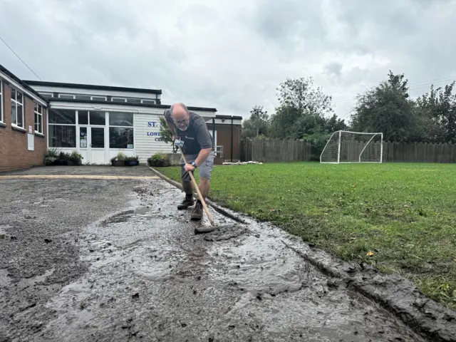 Site manager Derek Speake is using a brush to try and clear water and mud from a path leading to the front door of the school.