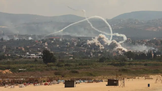 A general view of the skyline with mountains in the background and smoke billowing from rockets being fired over buildings in the foreground