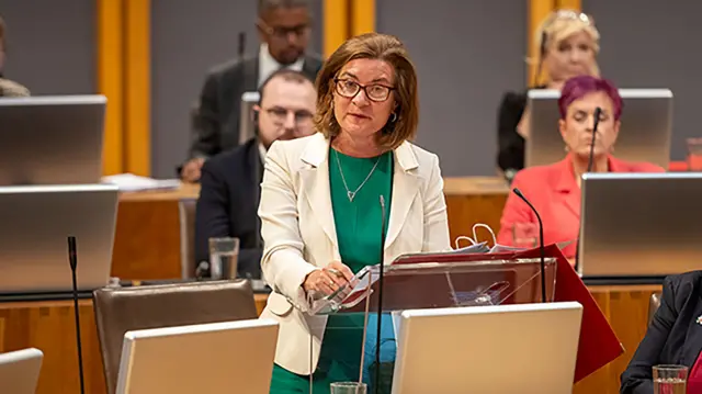 Eluned Morgan, wearing a green dress and white blazer, addresses the Senedd during First Minister's Questions (file photo)