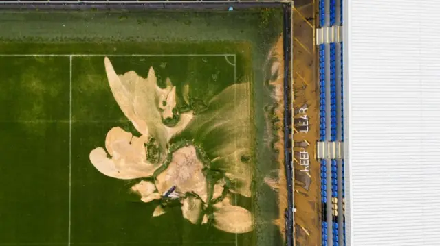 A sinkhole on the pitch and flooded walkways at the Cherry Red Records Stadium, home of AFC Wimbledon.