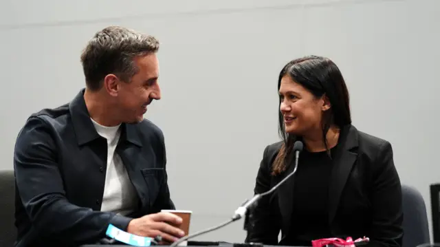 Gary Neville and Lisa Nandy smile at each other behind a microphone