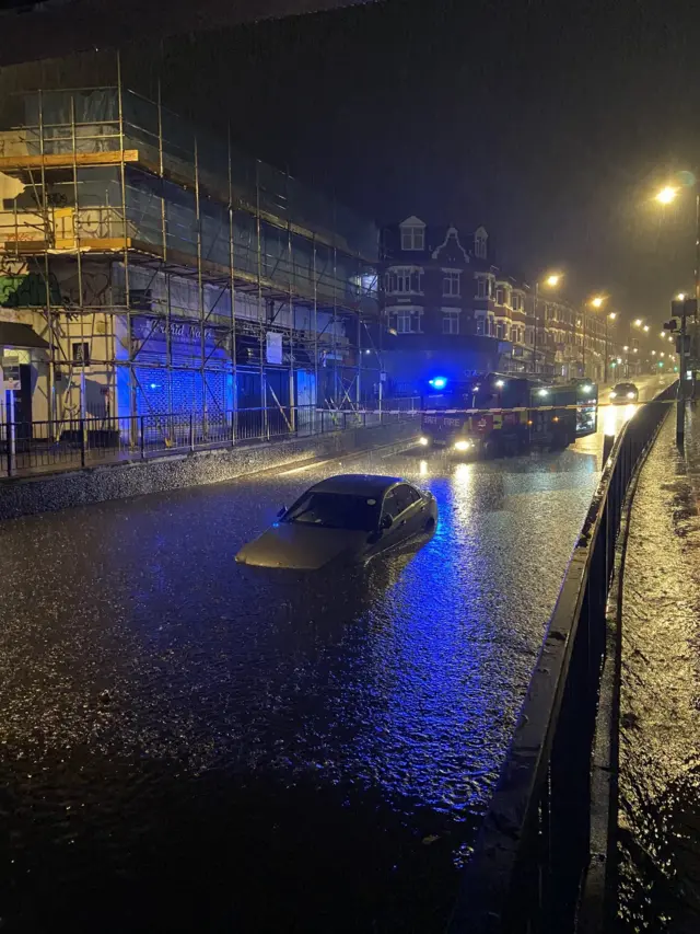 A car partially submerged in a large amount of floodwater on a dark street