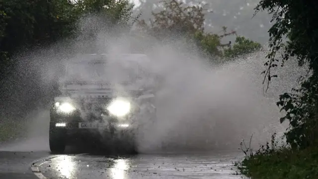 Cars drive through surface water in Willersey village, Gloucestershire.