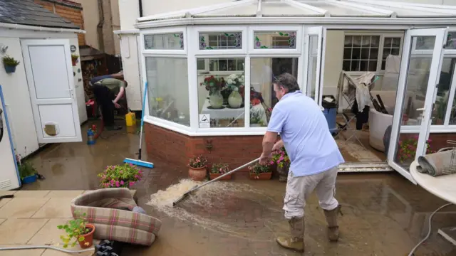 A man sweeps surface water away from a flooded garden