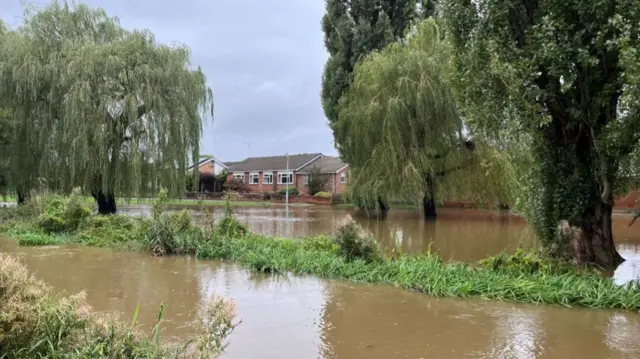 River threatening to overflow in Shefford. You can see the river approaching the banks, near some houses.