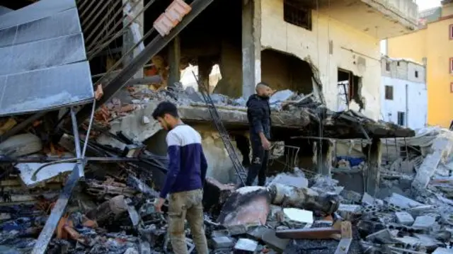 Two men stand on the rubble of a destroyed building.