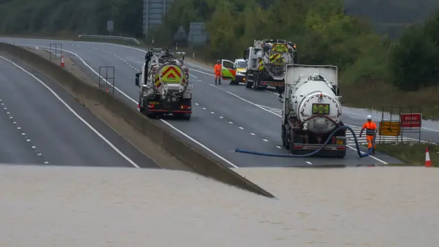 A picture of tankers on the A421 at the Marstone Moretaine Interchange in Bedfordshire. The road is flooded with the three vehicles parked close to the water. Pump lines can be seen on the road while workers in high-vis move about.