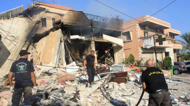 Rescuers work in front of a badly damaged building, which has a visible scorch mark on the front