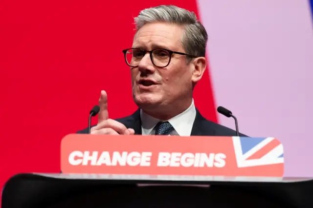 Starmer giving his speech at a lectern which says 'change begins'