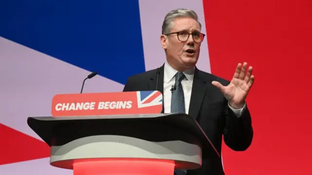 Sir Keir Starmer speaks from behind a podium at the Labour Party Conference. In the background is a huge Union Jack