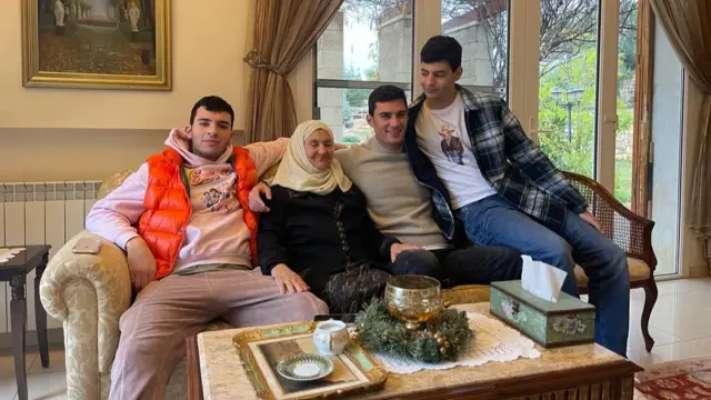 Rashad sits on a sofa in a lounge with his grandmother and two brothers.