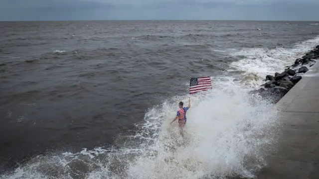 A drone view shows a person holding an American flag and being splashed by a crashing wave as Hurricane Helene intensifies before its expected landfall on Florida’s Big Bend, in Alligator Point, Florida, U.S. September 26, 2024.