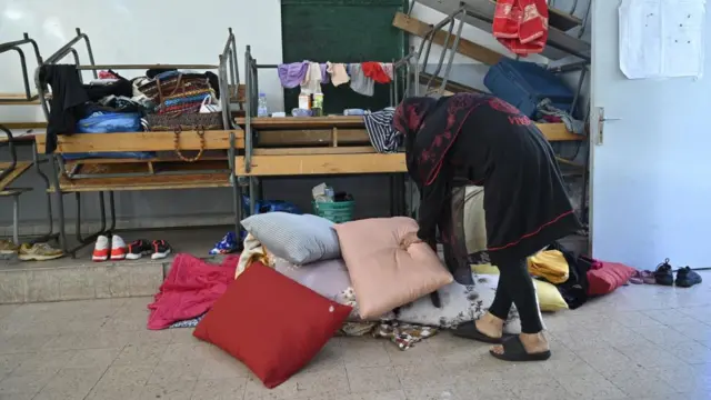 Woman piling up pillows at a makeshift shelter in an educational institution hosting Lebanese people who fled from southern Lebanon