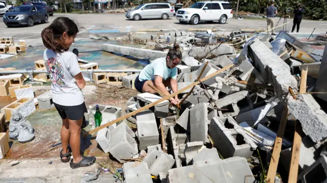 A girl looks on and her mother cleans up rubble from a collapsed building in Steinhatchee, Florida