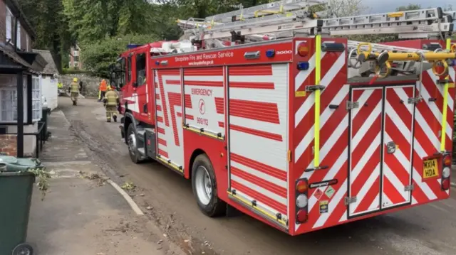 A fire engine in a street in All Stretton with firefighters in the distance