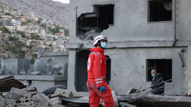 A member of the Lebanese Red Cross looks upwards against a backdrop of rubble and a hollowed out building