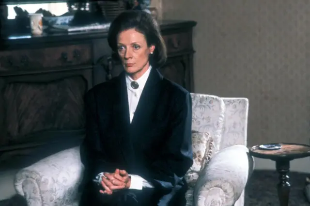 Maggie Smith sitting on a living room armchair