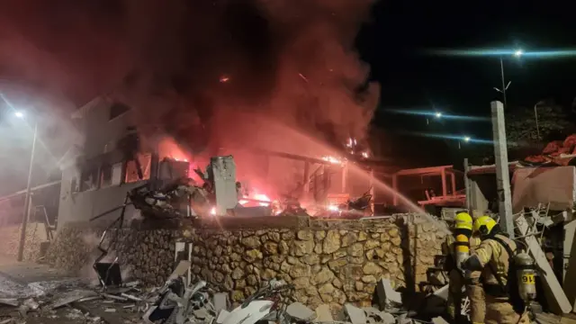 Firefighters spraying a burning house in Safed with a hose.