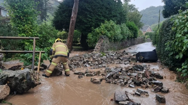 A firefighter tackles a collapsed wall as flood water  runs down the road