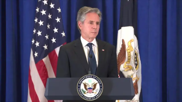 Antony Blinken during a press conference wearing a suit with an American flag behind him