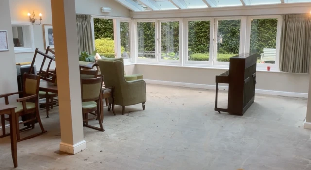 The ground floor of the care home with a piano, chairs and windows