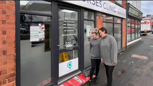 Two women stood outside a shop front with sand bags by the door