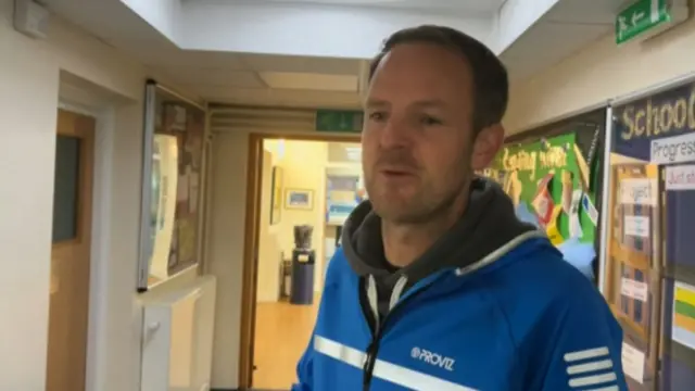 A man in a blue jecket, stood in a school corridor