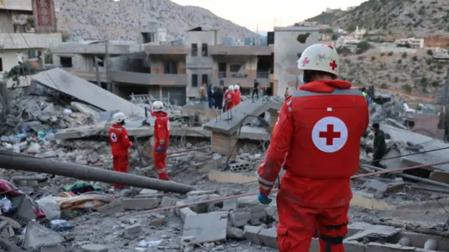 A few members of the Lebanese Cross stand in the rubble - collapsed and hollowed buildings can be seen