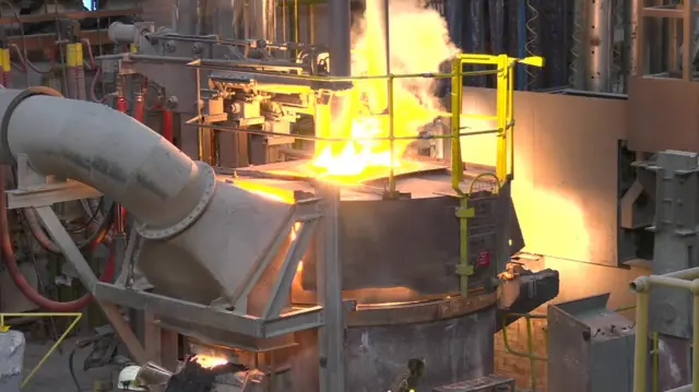 An electric arc furnace in action - it is a large mechanical device with flames coming out of the top