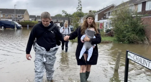 Jon House and his family - including his six-month-old son - evacuated from their home in Chaunterell Way. Jon can be seen holding the hand of his wife while they wade through the flood waters in Oxfordshire