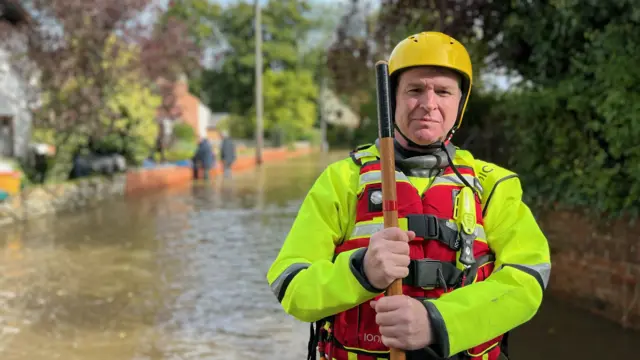 Richard McSweeney wearing a helmet, high visibility waterproofs and a lifejacket, carrying a staff