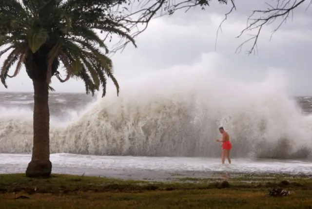 Tanner Flynn stands in shallow water near crashing waves as Hurricane Helene passes offshore on September 26, 2024, in St. Petersburg, Florid