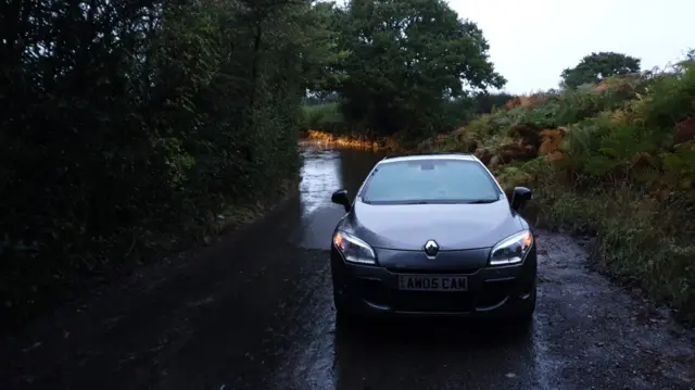 A car parked on a flooded road in the early hours of the morning