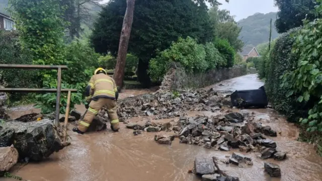 A firefighter trying to clear a flooded road with rocks strewn along it