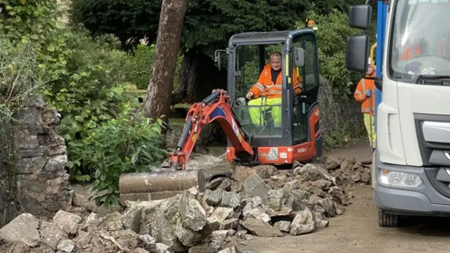 A small mechanical digger next to a lorry, moving blocks from a collapsed wall