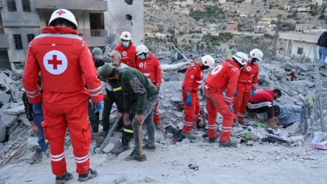 Members of the Lebanese Red Cross, dressed in red, search among rubble