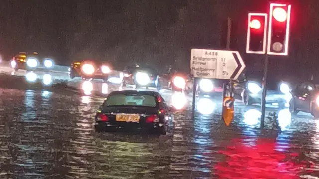 A black car submerged in water with queues of cars in the background