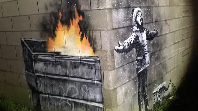 Banksy's Season's Greetings artwork in Port Talbot shows a young boy appearing to welcome snow with open arms, but the rest of the illustration on an adjoining wall shows it is in fact ash from a skip fire