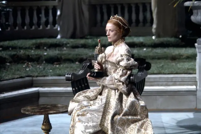 Maggie Smith on Stage in an elaborate dress holding a statue