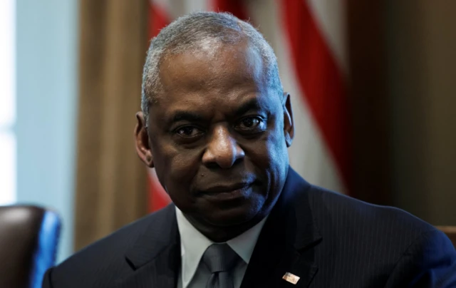 U.S. Secretary of Defense Lloyd Austin listens to Joe Biden during a cabinet meeting inside the West Wing of the White House. The USA flag can be seen in the background behind his head