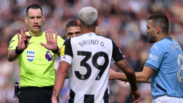 Bruno Guimaraes of Newcastle United interacts with Match Referee Jarred Gillett during the Premier League match between Newcastle United FC and Manchester City FC at St James' Park on September 28, 2024 in Newcastle upon Tyne, England.